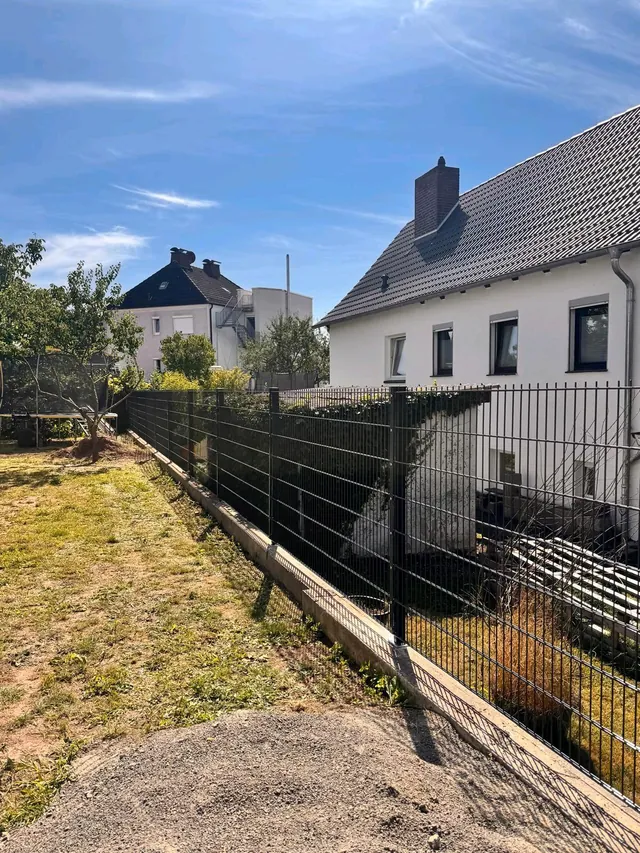 Doppelstabmattenzaun auf einem Betonsockel am Rand eines Hausgartens